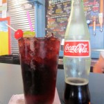 Mexican coca cola bottle next to a full glass with a cherry on top at Dat Dog Nola