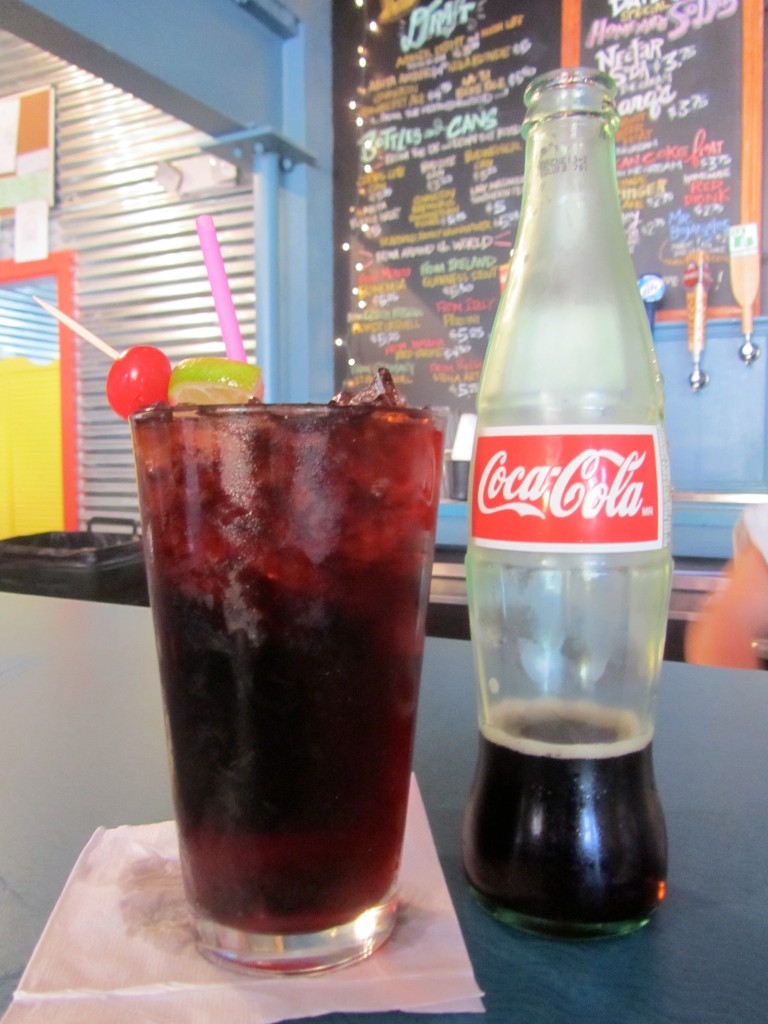 Mexican coca cola bottle next to a full glass with a cherry on top at Dat Dog Nola